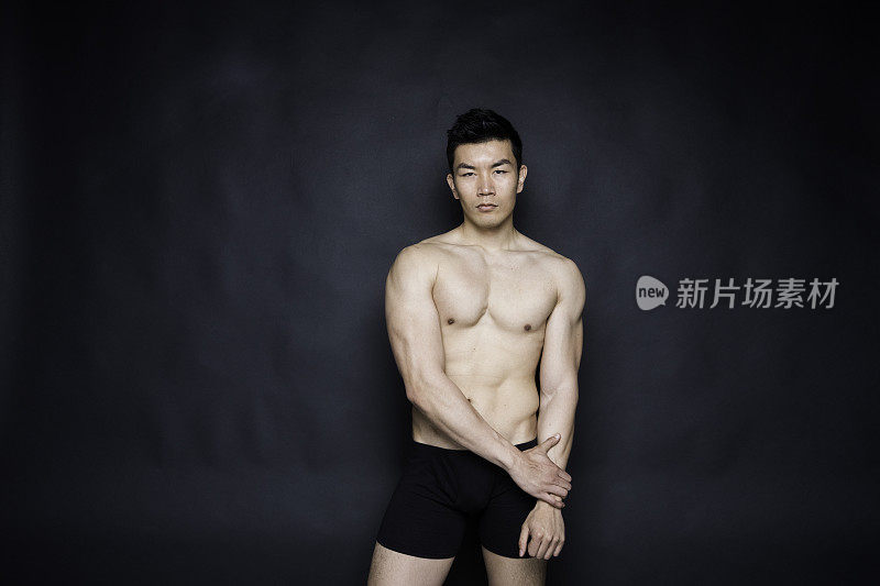 一名男子仅/腰部以上/正面20-29岁英俊的中国人/东亚民族男性站在黑色背景前，穿着衬衫/衬衫/内衣/男士内裤/半裙